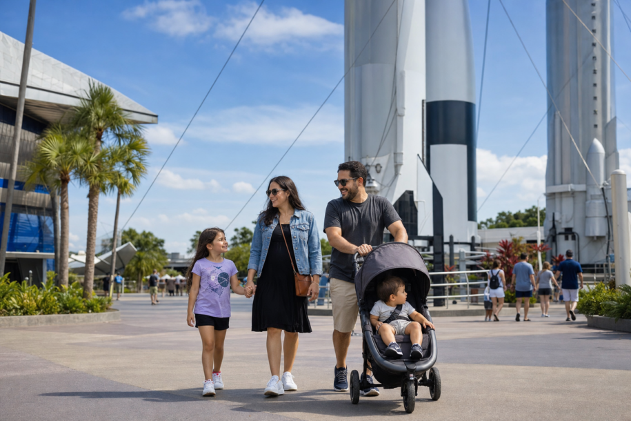 Family with a toddler walking toward a modern space exploration visitor complex on a sunny Florida day
